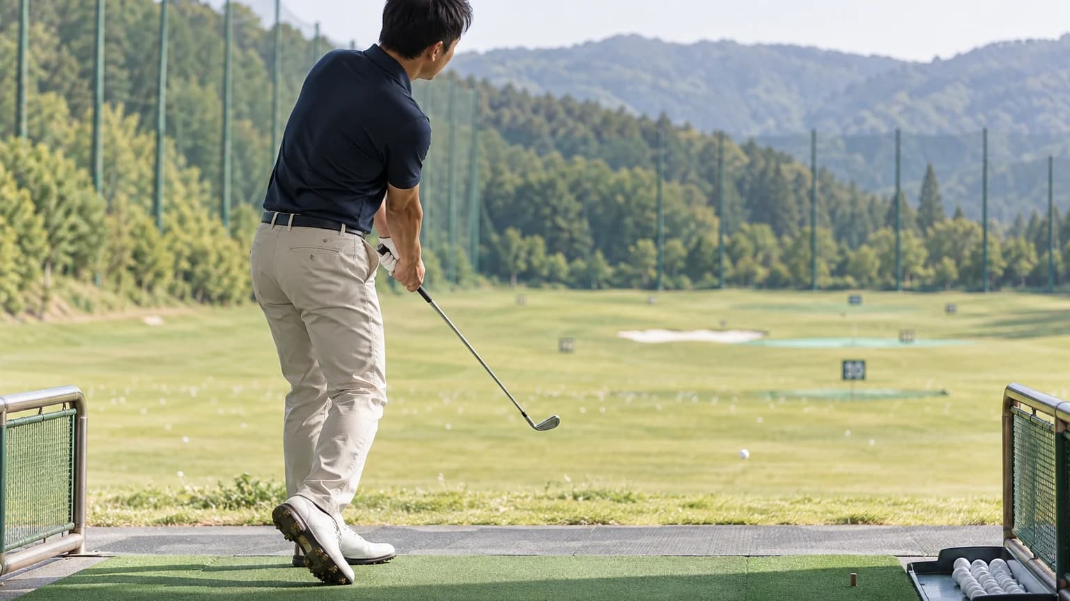 練習マットから出た低い打球を見届けるゴルファー