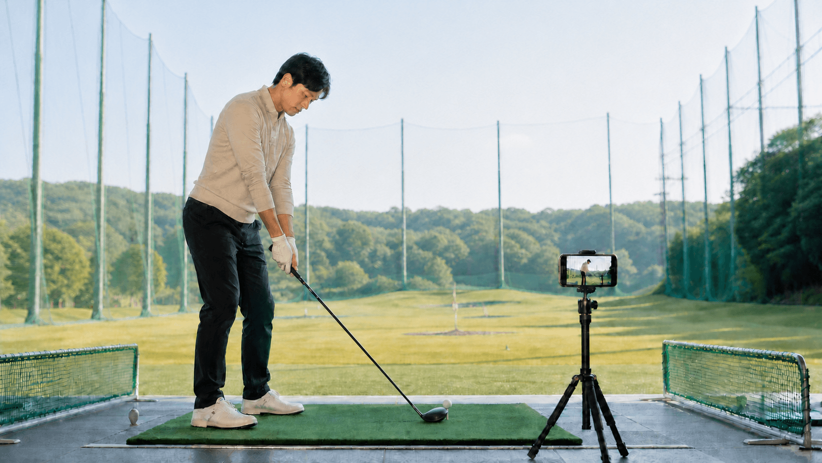 A golfer recording a swing with a smartphone mounted on a tripod at a driving range